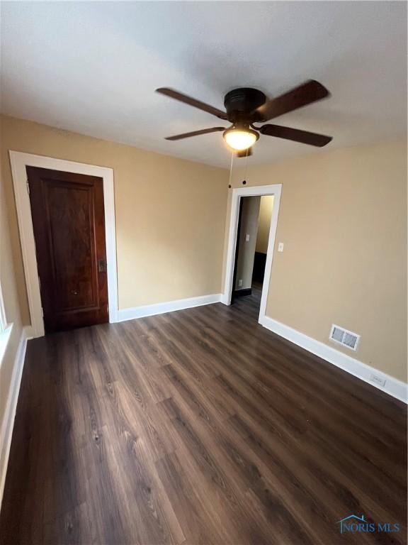 spare room featuring a ceiling fan, dark wood-style floors, baseboards, and visible vents