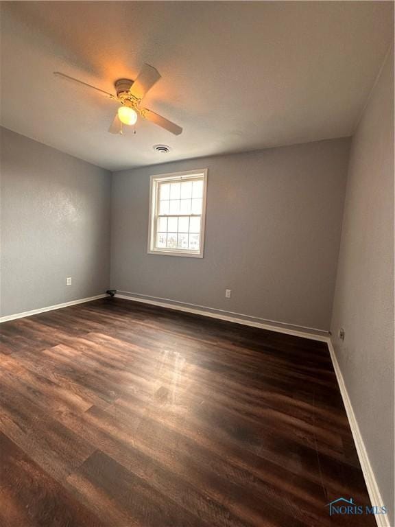 empty room featuring dark wood-style flooring, visible vents, ceiling fan, and baseboards