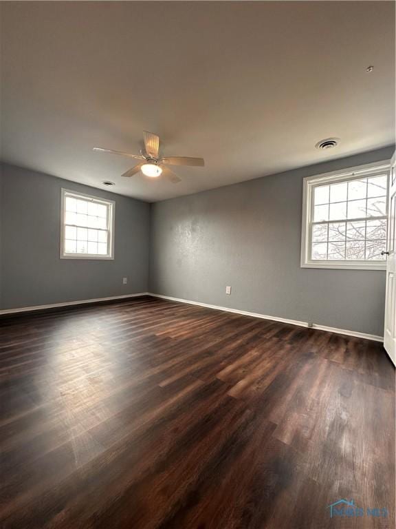 spare room featuring dark wood-type flooring, visible vents, ceiling fan, and baseboards