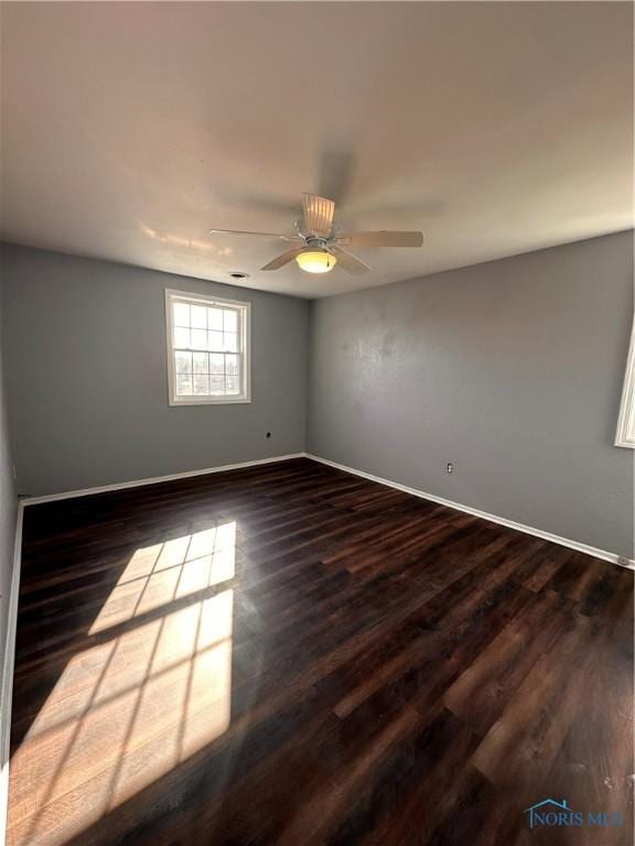 empty room featuring a ceiling fan, baseboards, and dark wood-type flooring