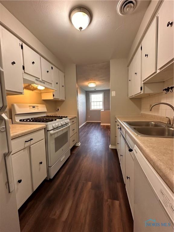 kitchen featuring under cabinet range hood, white appliances, a sink, white cabinetry, and dark wood-style floors