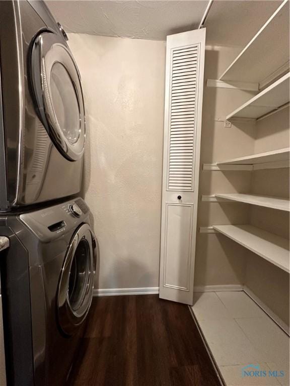 clothes washing area featuring laundry area, baseboards, dark wood-style floors, and stacked washer / dryer