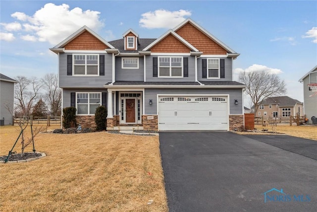 craftsman-style house featuring a garage, driveway, stone siding, fence, and a front yard