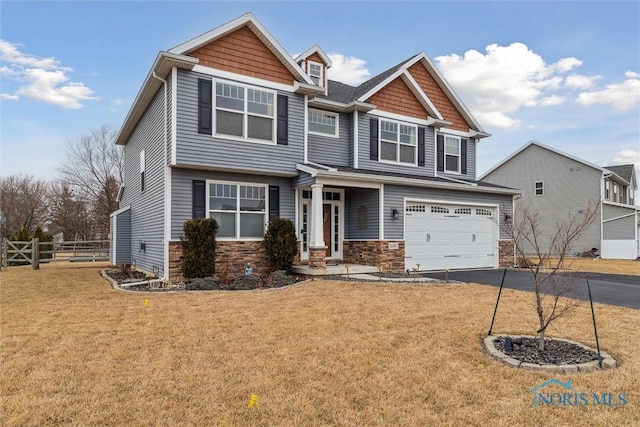 craftsman inspired home featuring a garage, fence, stone siding, driveway, and a front lawn