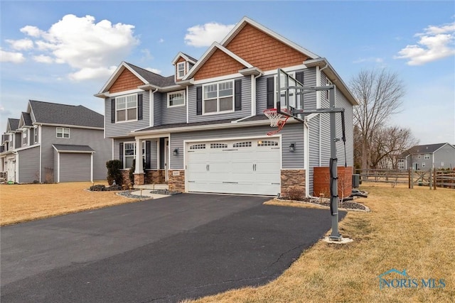 craftsman house featuring aphalt driveway, stone siding, fence, and a garage