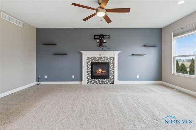 unfurnished living room with carpet, visible vents, a tiled fireplace, ceiling fan, and baseboards