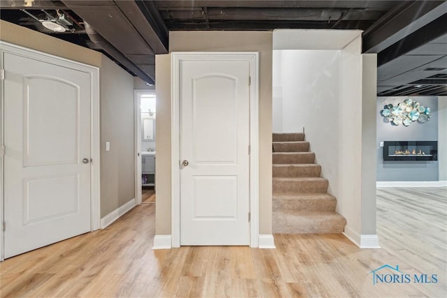 stairway featuring baseboards, wood finished floors, and a glass covered fireplace