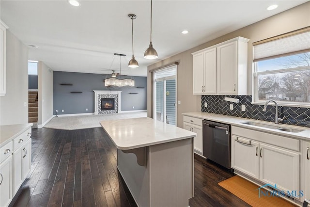 kitchen featuring a fireplace, a sink, white cabinets, stainless steel dishwasher, and backsplash