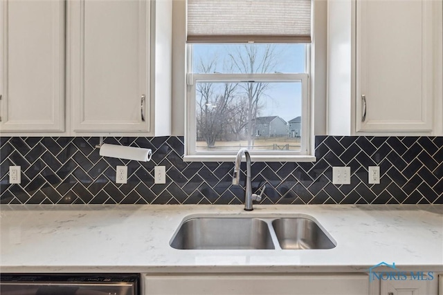 kitchen with stainless steel dishwasher, a sink, white cabinetry, and decorative backsplash