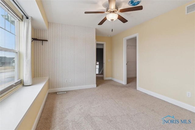 carpeted spare room featuring visible vents, ceiling fan, baseboards, and wallpapered walls