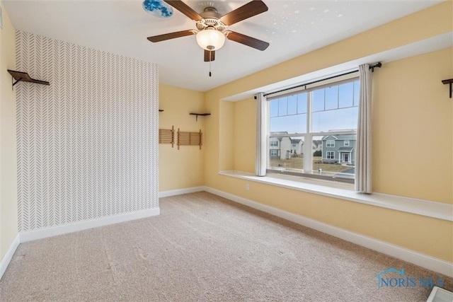 carpeted spare room with a ceiling fan, an accent wall, visible vents, and baseboards