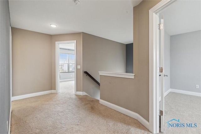 hallway featuring carpet floors, baseboards, and an upstairs landing