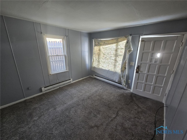 empty room featuring a healthy amount of sunlight, a baseboard radiator, and dark colored carpet