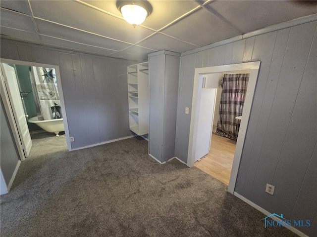 unfurnished bedroom featuring carpet flooring, wood walls, and ensuite bathroom