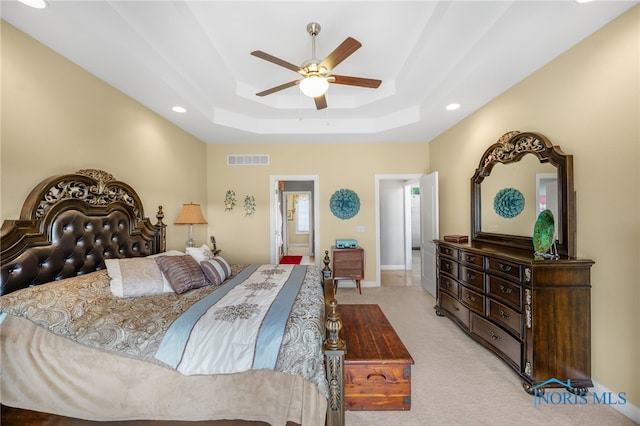 bedroom with ceiling fan, light colored carpet, visible vents, baseboards, and a tray ceiling