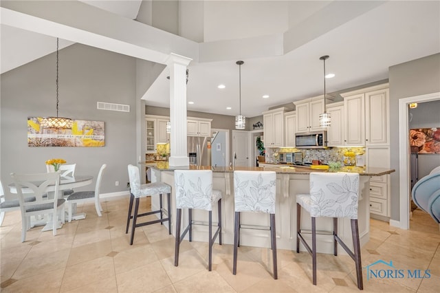 kitchen featuring visible vents, decorative backsplash, a high ceiling, stainless steel appliances, and a kitchen bar