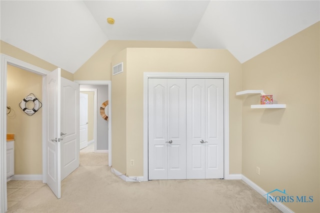 unfurnished bedroom with lofted ceiling, light colored carpet, visible vents, baseboards, and a closet