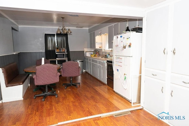 kitchen featuring a wainscoted wall, range with electric stovetop, breakfast area, freestanding refrigerator, and a sink