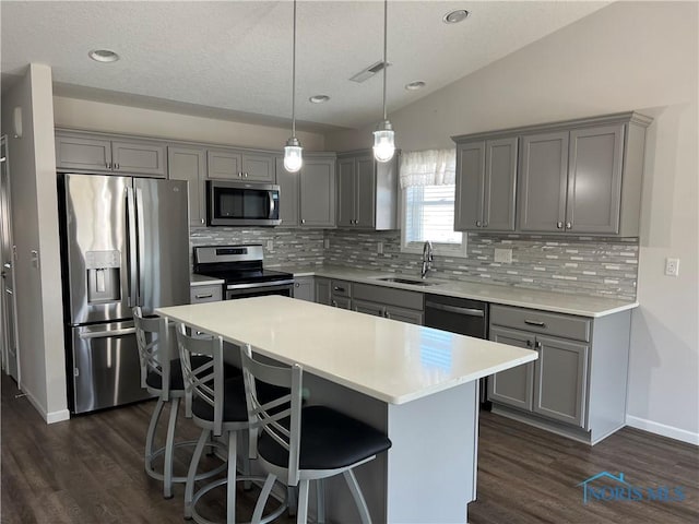 kitchen featuring a kitchen island, lofted ceiling, gray cabinets, a sink, and appliances with stainless steel finishes