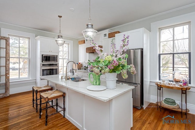 kitchen with appliances with stainless steel finishes, light stone counters, wood finished floors, white cabinetry, and a sink