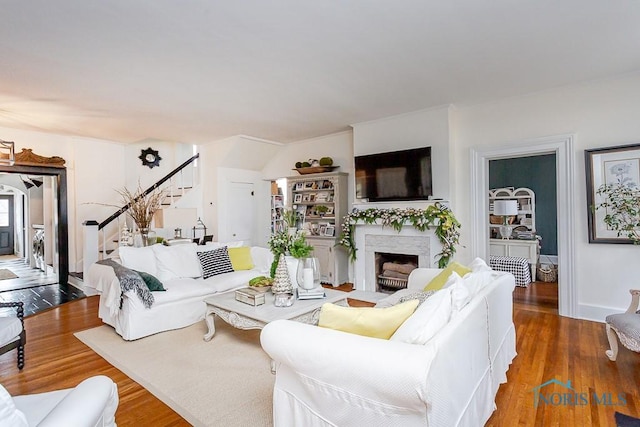 living room featuring stairs, baseboards, a fireplace, and wood finished floors