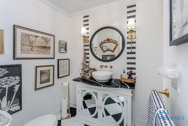 half bathroom featuring toilet, baseboards, crown molding, and vanity