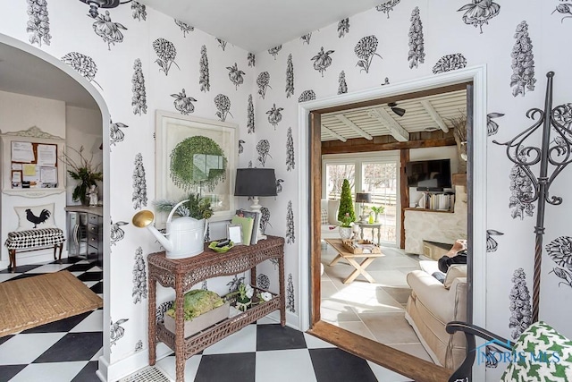 doorway to outside with wallpapered walls, a fireplace, arched walkways, and tile patterned floors