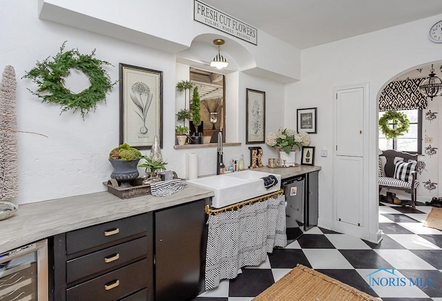 kitchen featuring arched walkways, dark floors, beverage cooler, a sink, and light countertops