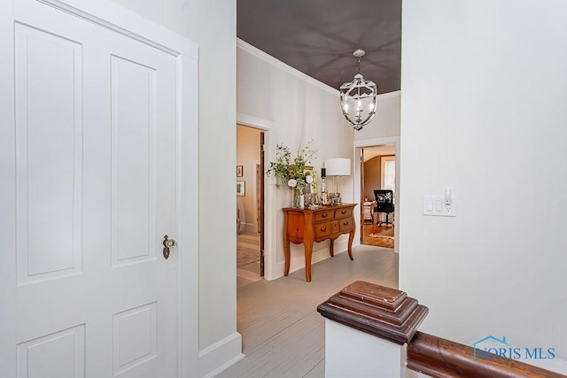 corridor with a chandelier, ornamental molding, and light wood finished floors