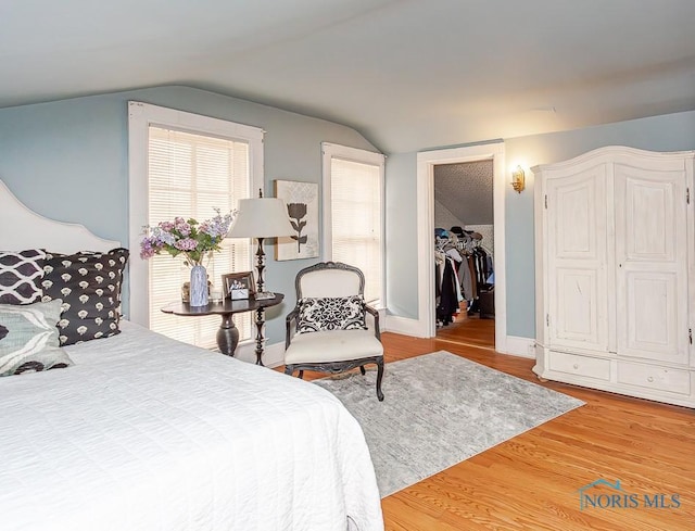 bedroom with a walk in closet, baseboards, vaulted ceiling, and wood finished floors