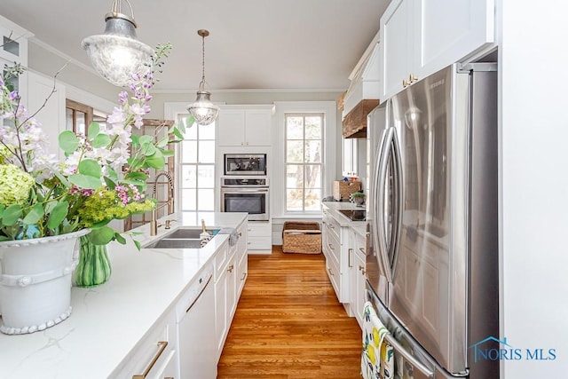 kitchen with stainless steel appliances, a sink, white cabinetry, ornamental molding, and light wood-type flooring