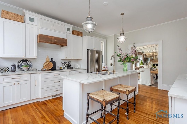 kitchen with black electric stovetop, white cabinets, a kitchen breakfast bar, freestanding refrigerator, and light wood finished floors