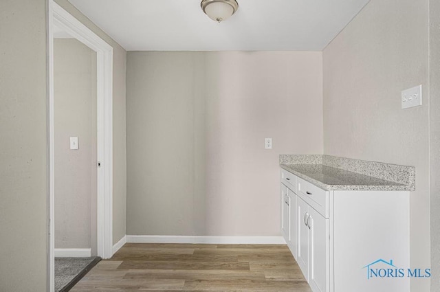 interior space with baseboards, white cabinetry, and light wood finished floors