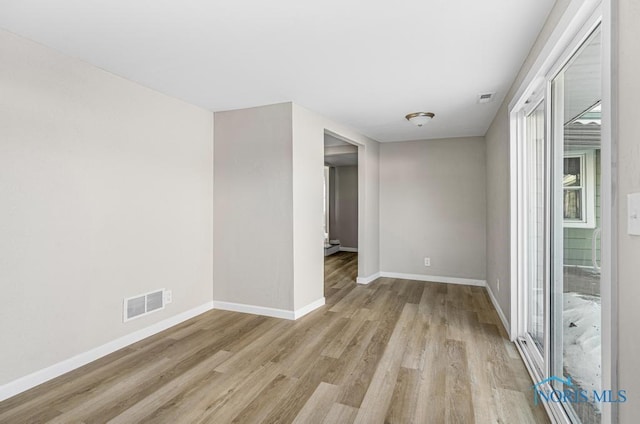 empty room with visible vents, light wood finished floors, and baseboards