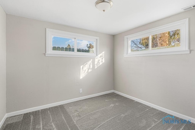 empty room with carpet, visible vents, and baseboards