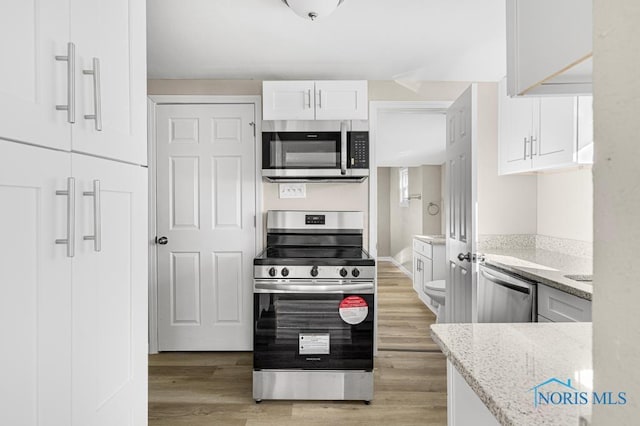 kitchen featuring appliances with stainless steel finishes, white cabinetry, light wood-style floors, and light stone counters