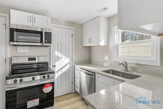 kitchen with white cabinets, light stone countertops, stainless steel appliances, and a sink