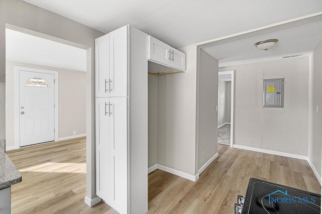 corridor featuring light wood-type flooring, electric panel, and baseboards