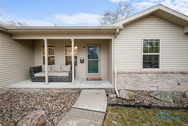 view of exterior entry with a porch, crawl space, and brick siding