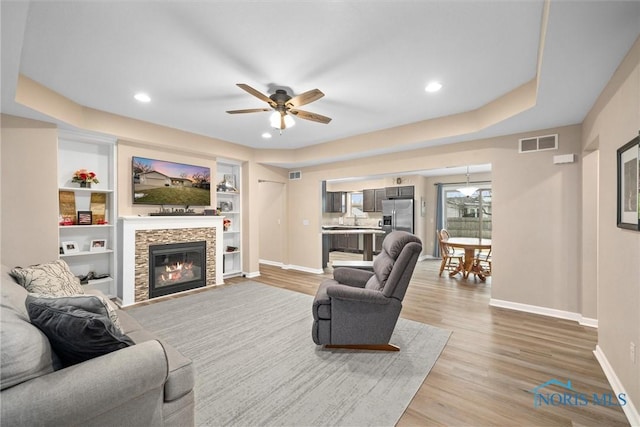 living area with visible vents, a stone fireplace, baseboards, and wood finished floors