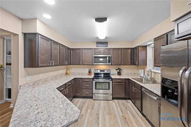 kitchen with light wood-style floors, appliances with stainless steel finishes, dark brown cabinets, and a sink