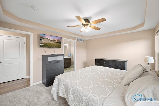 bedroom featuring a raised ceiling, light colored carpet, visible vents, and baseboards