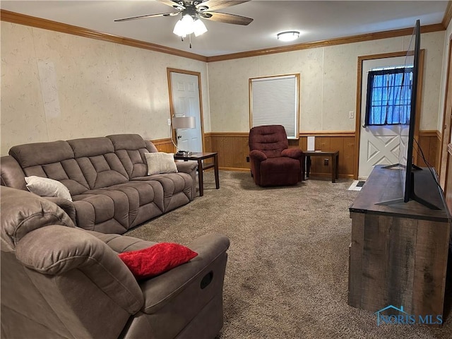 living room with a wainscoted wall, ceiling fan, ornamental molding, and carpet