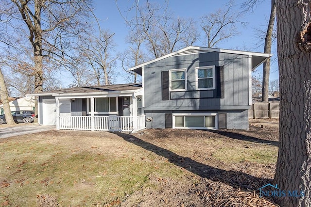 tri-level home with driveway, a porch, an attached garage, and fence