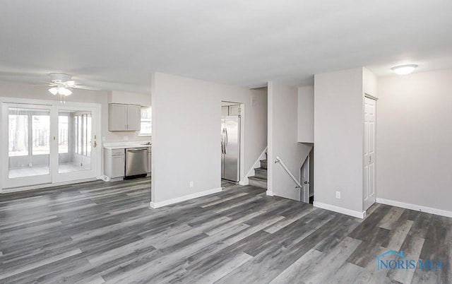 unfurnished living room featuring dark wood-style floors, baseboards, and stairway