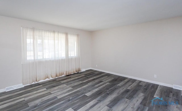 empty room featuring dark wood-style floors, baseboards, and visible vents