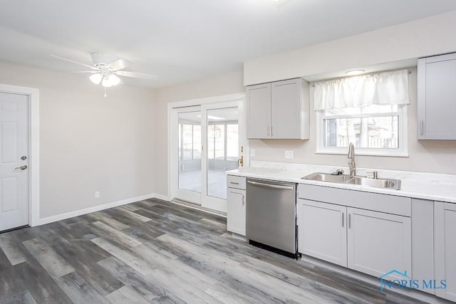 kitchen featuring baseboards, wood finished floors, light countertops, stainless steel dishwasher, and a sink