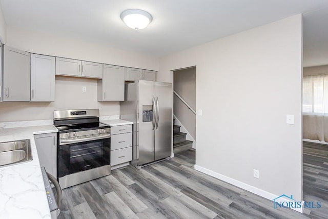 kitchen featuring light wood-type flooring, baseboards, appliances with stainless steel finishes, and gray cabinets