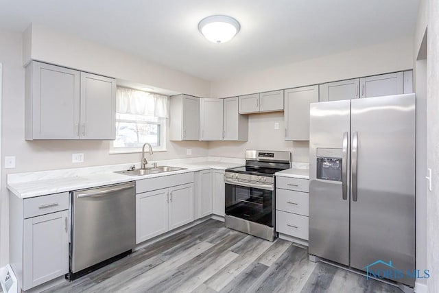 kitchen featuring appliances with stainless steel finishes, gray cabinets, light countertops, light wood-style floors, and a sink