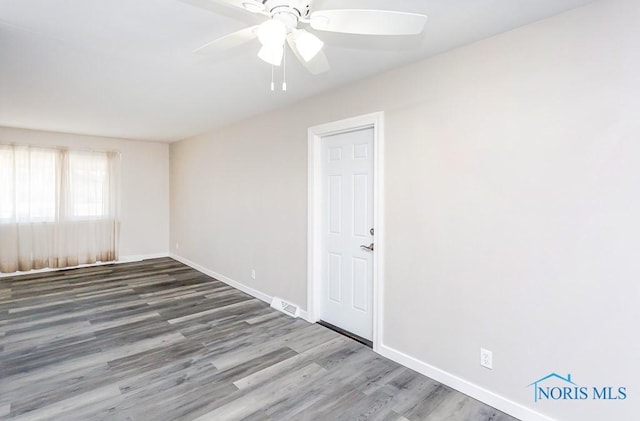 spare room featuring a ceiling fan, visible vents, baseboards, and wood finished floors